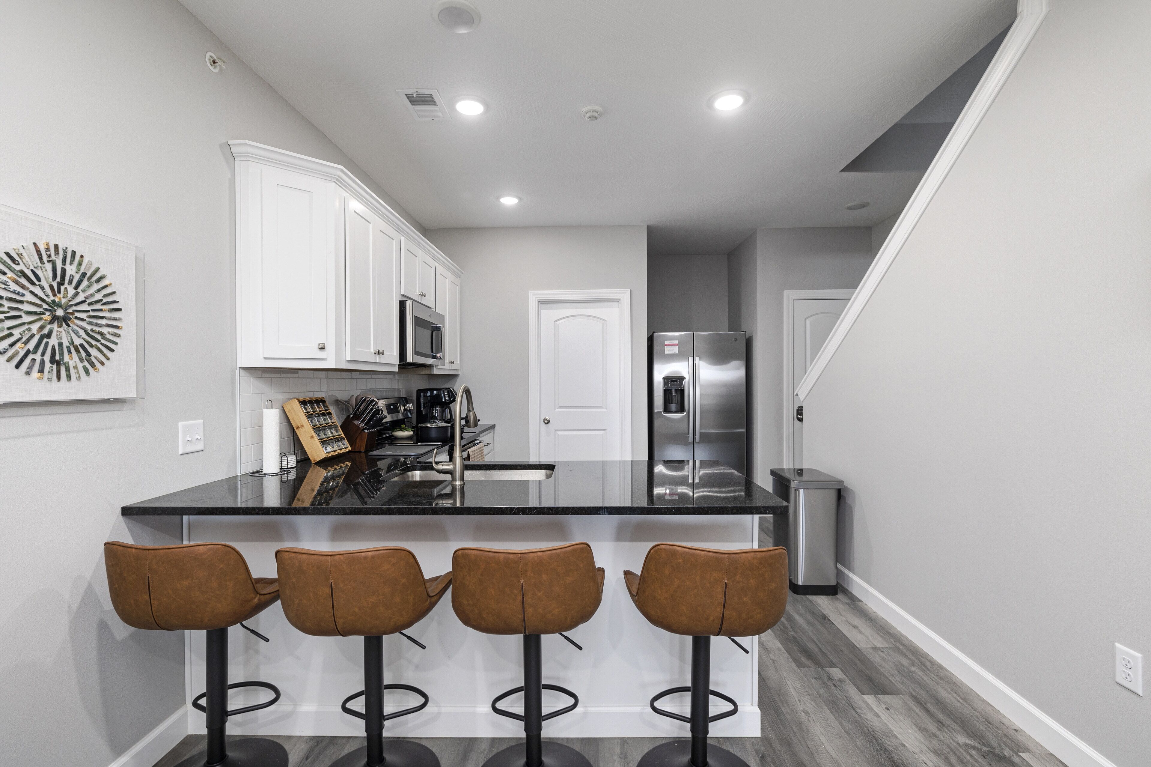 A modern kitchen with white cabinets, a stainless steel refrigerator, and a black countertop.