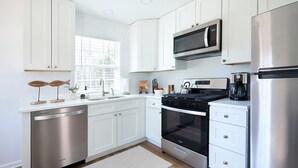 A modern kitchen with white cabinets, stainless steel appliances, and a window providing natural light.