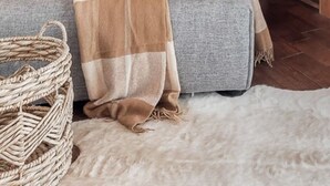 A cozy log cabin room with a sofa, pillows, a blanket, a woven basket, and a hanging light fixture.