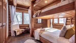 A cozy cabin room with a bunk bed, wooden walls, and a large window.