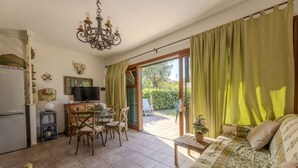 A cozy living room with a sofa, a dining table with chairs, a television, and a chandelier. - VILLINO LA POLVERIERA (Porto Azzurro)