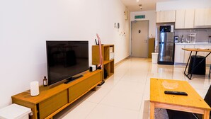 Ein modernes Wohnzimmer mit Flachbildfernseher, Holzmöbeln, einem kleinen Esstisch und einer Küchenzeile mit Kühlschrank und Mikrowelle.
