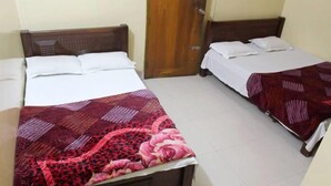 Dos camas individuales con cabeceros de madera y ropa de cama blanca, una con colcha estampada roja y rosa y la otra con colcha roja y blanca.