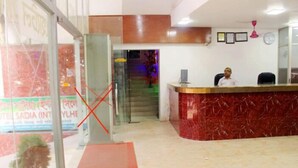 Zona de recepción de un hotel con mostrador de mármol, una recepcionista y una escalera que sube a los pisos superiores.