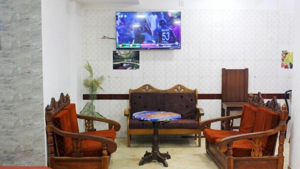 Una sala de estar con dos sillones de madera, un sofá, una mesita y un televisor montado en la pared.