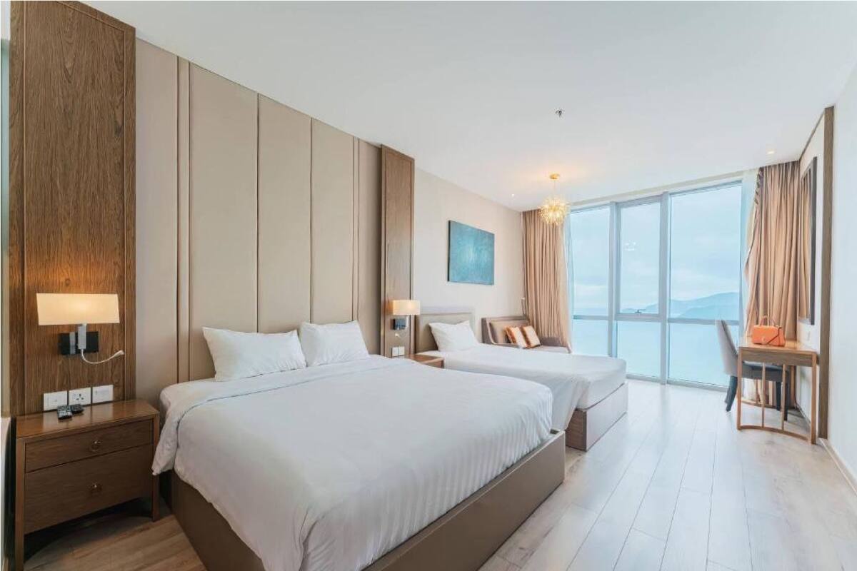 Une chambre d’hôtel avec deux lits, un bureau, une chaise et une grande fenêtre donnant sur un paysage agréable.