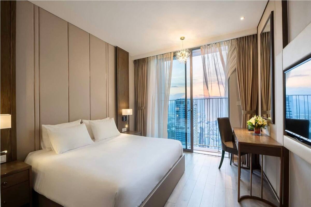 Une chambre d’hôtel avec un grand lit, un bureau avec une chaise, une télévision et un balcon offrant une vue sur la ville.