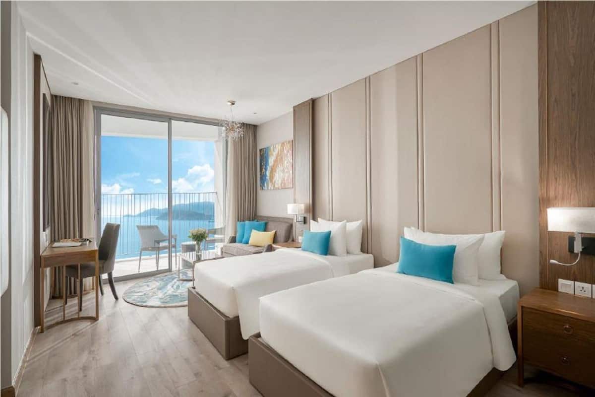 Une chambre d’hôtel avec deux lits, un bureau, une chaise et un balcon donnant sur la mer.