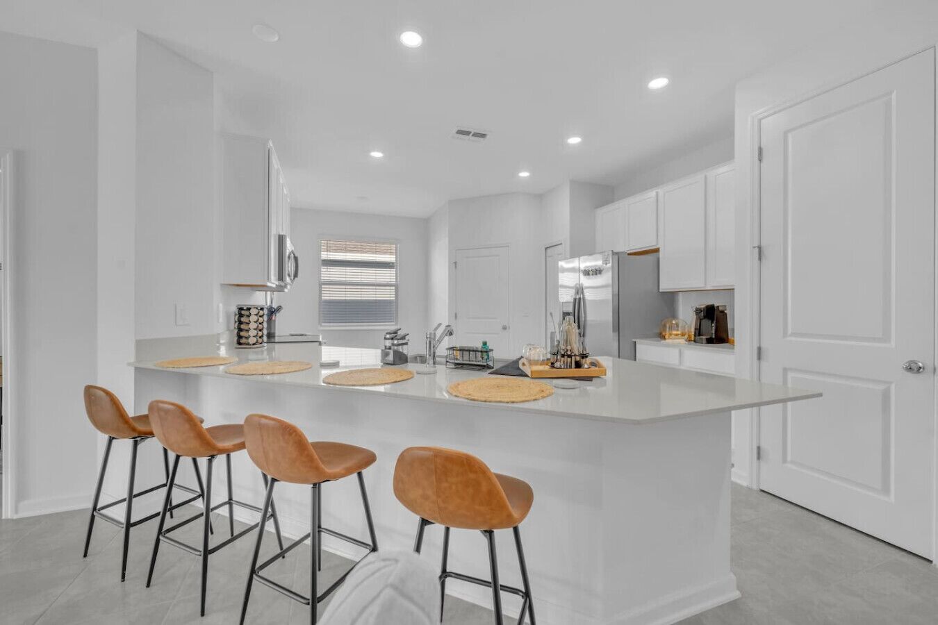Una cocina moderna con una isla central, taburetes de bar y muebles blancos.
