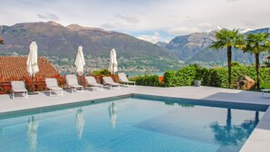 A pool with lounge chairs and umbrellas, surrounded by greenery and mountains in the background. - Residenza Miralago Apt. D32 by Interhome (Piazzogna)
