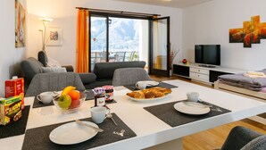 A modern living room with a dining area, a sofa, a TV, and a balcony with a mountain view. - Residenza Miralago Apt. D32 by Interhome (Piazzogna)