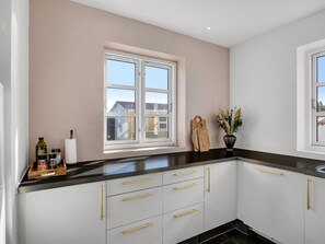 Une cuisine moderne avec des meubles blancs, un plan de travail noir et une fenêtre donnant sur des maisons.