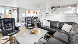 A modern living room with a leather sofa, a dining area with chairs, and a large window providing natural light.