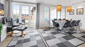 A modern dining room with a checkered floor, a dining table with chairs, a sofa, and a view of the outside through large windows.