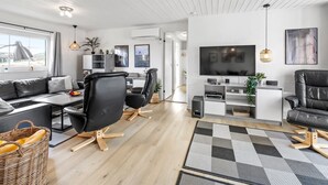 A modern living room with a sofa, chairs, a TV, and a dining area.