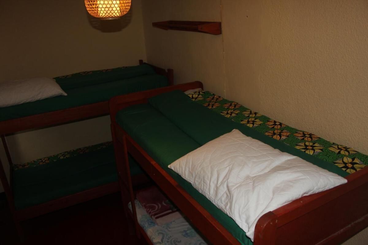 Une chambre avec deux lits superposés, chacun doté d’un matelas vert et d’oreillers blancs. Une étagère est fixée au mur au-dessus des lits.