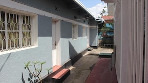 A narrow, covered walkway leading to a building with a blue exterior and white trim. - Room in B&B - Amahoro Guest House - 6-bed Mixed Dormitory Room no1 (Muhoza)