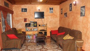A living room with two patterned sofas, a coffee table, a bookshelf, a television, and a drum. - Room in B&B - Amahoro Guest House - 6-bed Mixed Dormitory Room no1 (Muhoza)