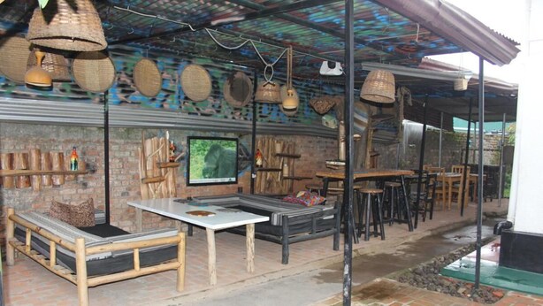 An outdoor seating area with wooden furniture, a television, and decorative baskets. - Room in B&B - Amahoro Guest House - Double Room With Private Shower Room (Muhoza)