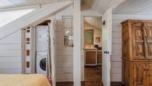 Une chambre à coucher comprenant un lit, une armoire en bois, un lave-linge et une salle de bain avec un lavabo et un miroir.