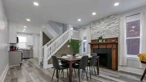 A spacious living area with a dining table, chairs, a staircase, a kitchen, and a fireplace.