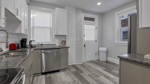 A modern kitchen with stainless steel appliances, white cabinetry, and a grey floor.