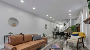 A modern living room with a brown leather sofa, a coffee table, and a dining area with chairs and a table.