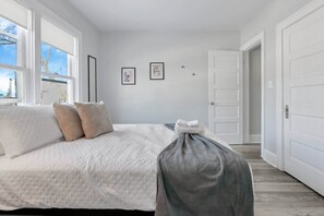 A bedroom with a bed, white walls, framed pictures, and a door.