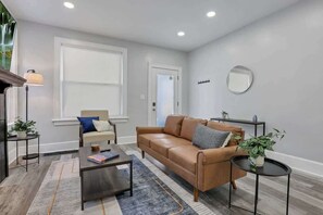 Un salon avec un canapé en cuir marron, une petite table basse, une table d’appoint, une lampe et une plante en pot.