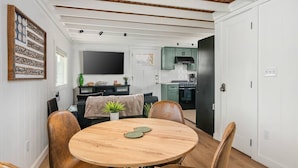 Eine moderne Küche mit Fernseher, ein Essbereich mit rundem Tisch und Stühlen sowie ein Wohnzimmer mit Sofa und Wanddeko.