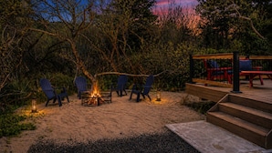 Ein Feuerkorb umgeben von Stühlen, eine Holzterrasse mit roten Sesseln und eine Treppe nach oben.