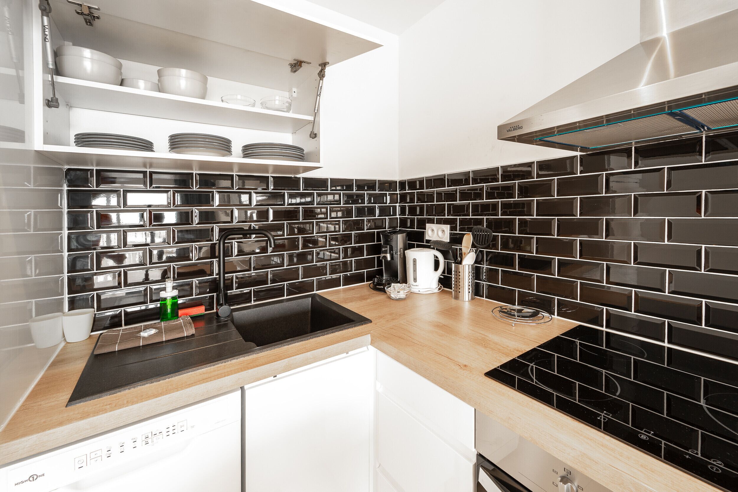 A modern kitchen with black and white tiles, a built-in dishwasher, and a coffee maker.