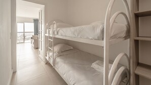 Habitación con literas, ropa de cama blanca y una estantería de madera.