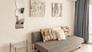 Una sala de estar moderna con un sofá gris, dos obras de arte, un espejo y una mesa de vidrio.