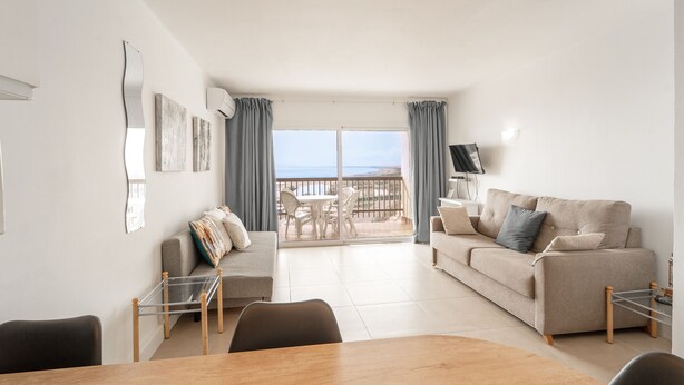 Una sala de estar moderna con sofá, una mesa de comedor y un balcón con vista al mar.
