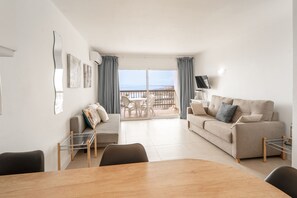 Una sala de estar moderna con sofá, una mesa de comedor y un balcón con vista al mar.