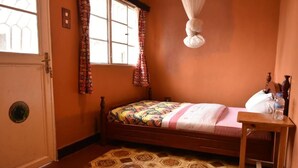 A small, cozy room with a single bed, a wooden nightstand, a window with patterned curtains, and a unique ceiling light fixture.