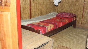 Une petite chambre avec un lit simple, un mur en bambou et un sol recouvert d’un tapis tissé.