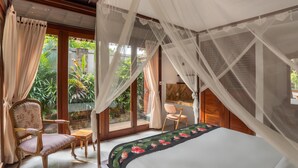 A bedroom with a bed, a chair, a small table, and a large window with a view of greenery. - The Jema Villa Ubud (Ubud)
