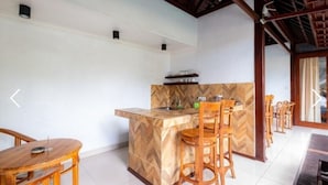 A compact kitchen with a herringbone-patterned backsplash, wooden bar stools, and a dining table with chairs. - The Jema Villa Ubud (Ubud)
