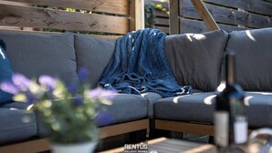 Une terrasse en bois avec un canapé gris et une couverture bleue.