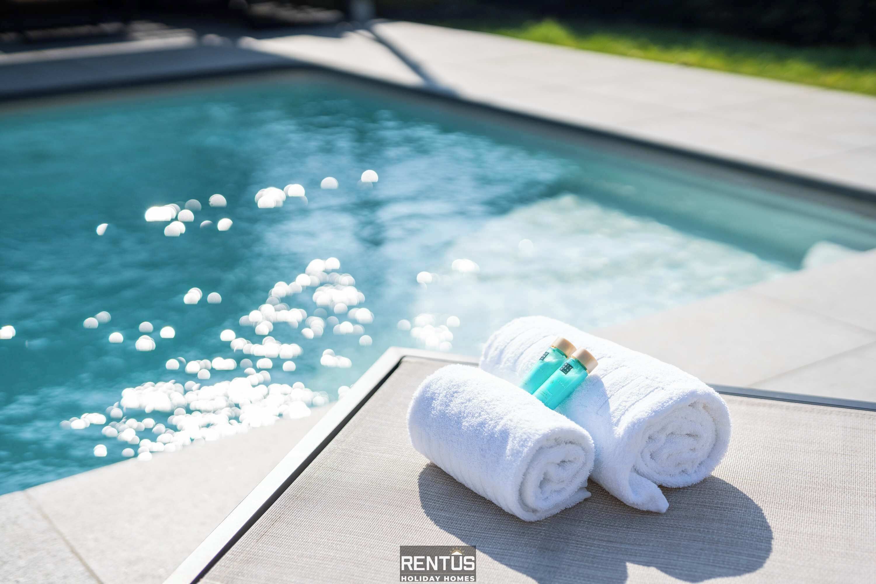 A poolside area with two rolled towels and a bottle, suggesting a relaxing setting.
