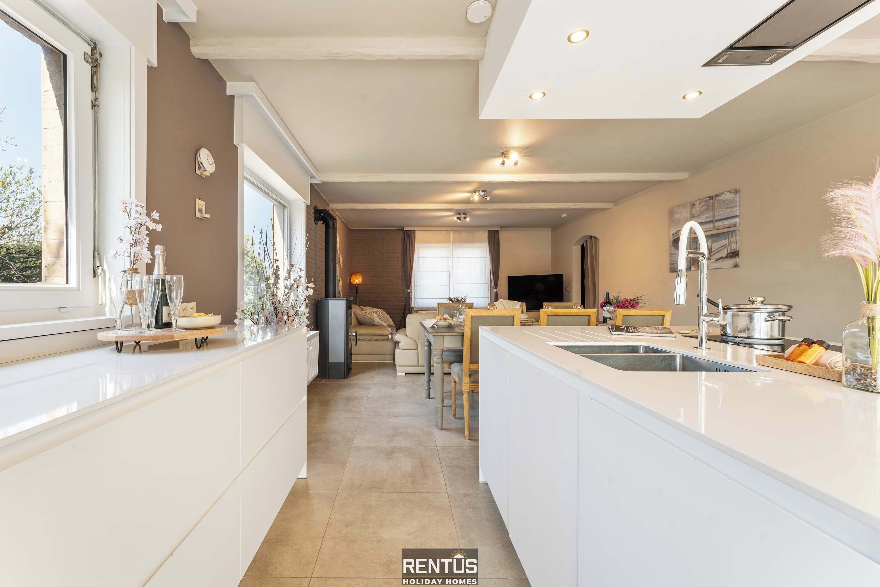 A modern kitchen with a central island, a dining area with a sofa, and a TV in the background.