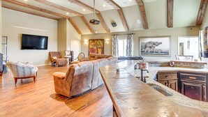 A spacious living area with a long wooden bench, a leather sofa, and a television mounted on the wall. - Spacious Edmond Vacation Rental w/ Shared Pool! (Edmond)