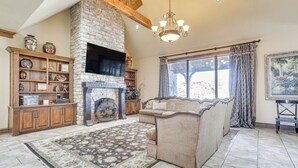 A living room with a stone fireplace, wooden cabinets, a sofa, and a large window with curtains. - Spacious Edmond Vacation Rental w/ Shared Pool! (Edmond)