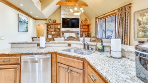 A spacious kitchen with granite countertops, wooden cabinets, a stone fireplace, and a large window with curtains. - Spacious Edmond Vacation Rental w/ Shared Pool! (Edmond)