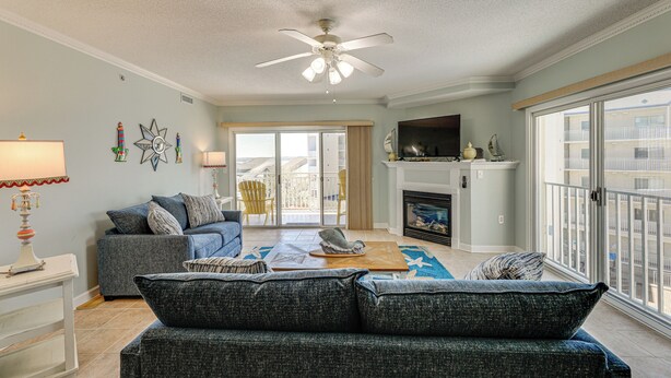 Ein Wohnzimmer mit Deckenventilator, Kamin, Sofa und Blick auf den Balkon.