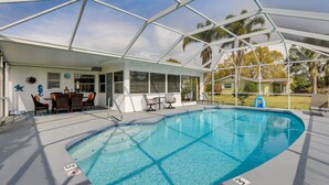 A covered swimming pool with a glass ceiling, lounge chairs, and a patio area with outdoor seating.