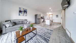 Un salon moderne avec un canapé gris, une table basse et une cuisine en arrière-plan.