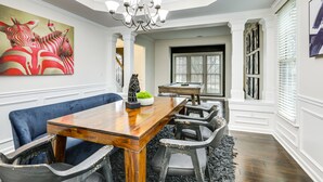 A dining room with a wooden table, black chairs, a blue bench, a chandelier, and a zebra painting on the wall. - Modern Stone Mountain Home w/ Spacious Deck, Grill (Stone Mountain)